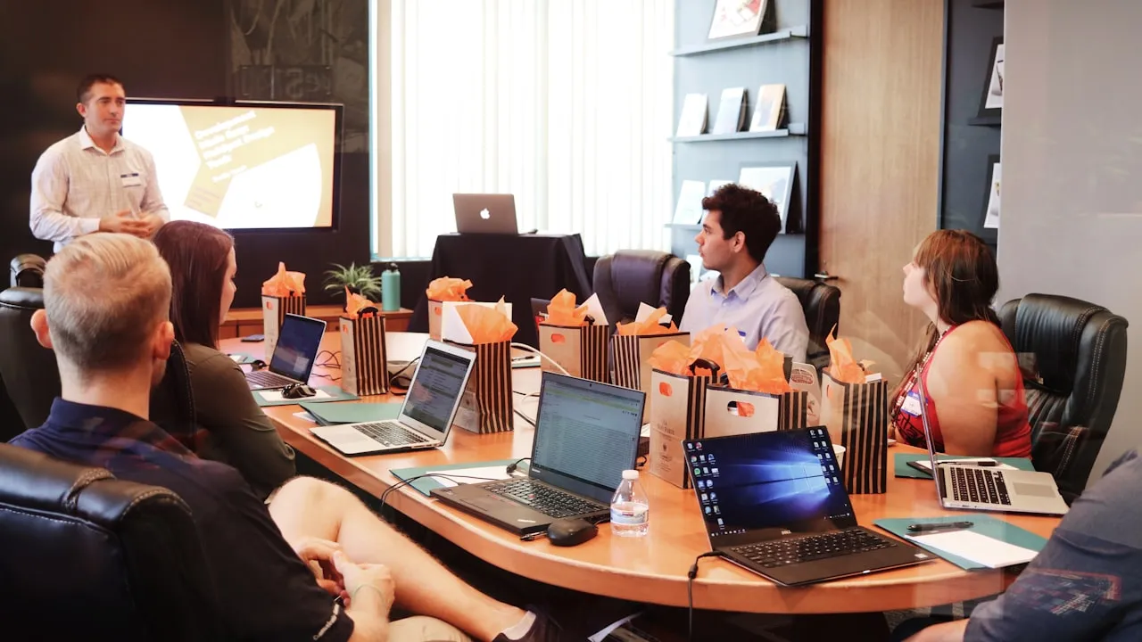 A presenter and team around a boardroom table with laptops