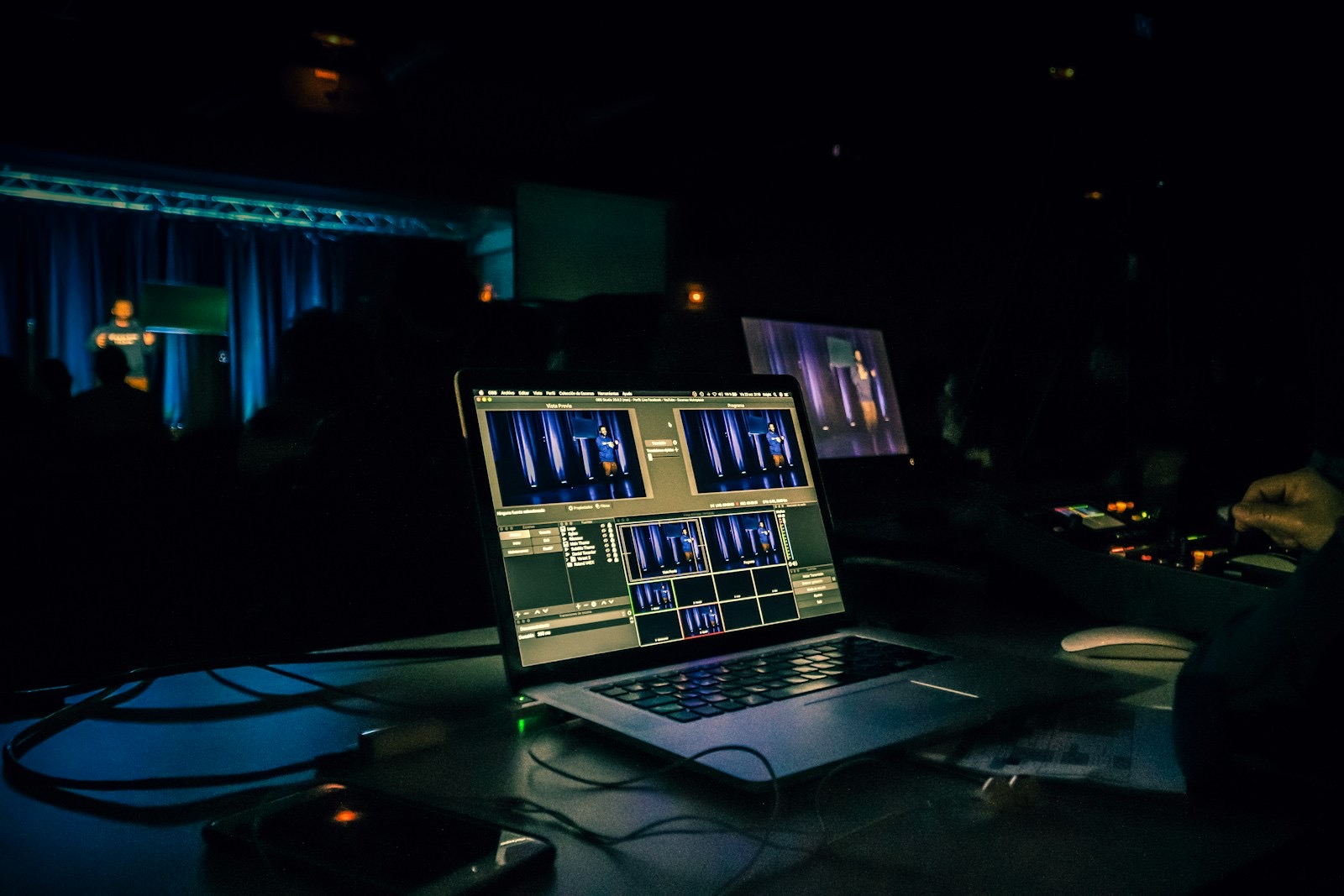 A laptop at a dark venue tech desk with the stage behind it