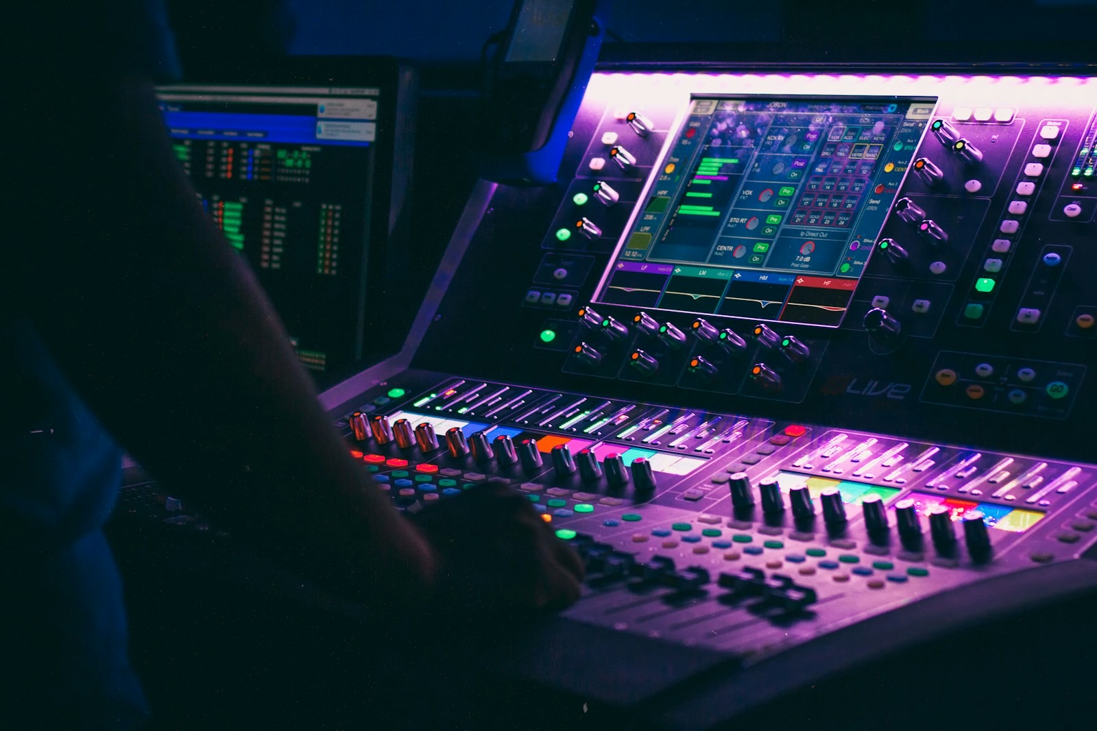 A venue engineer's hand on a lit touchscreen mixing console