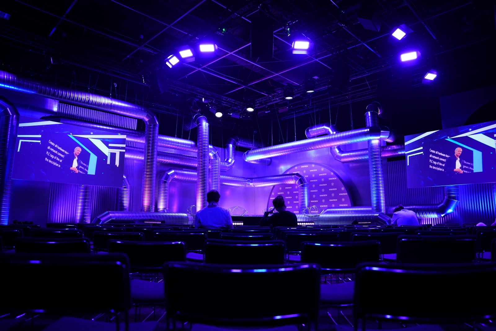 A violet-lit conference stage with screens, seats in front