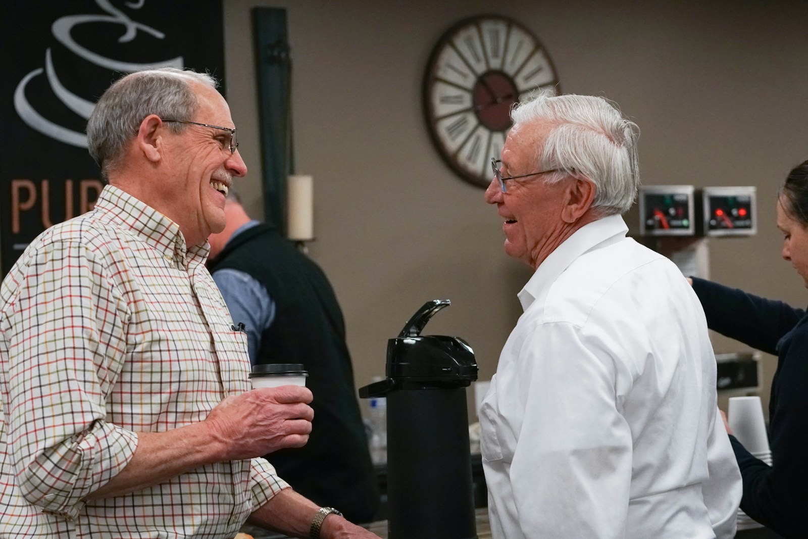 Two older men laughing over coffee in the church lobby
