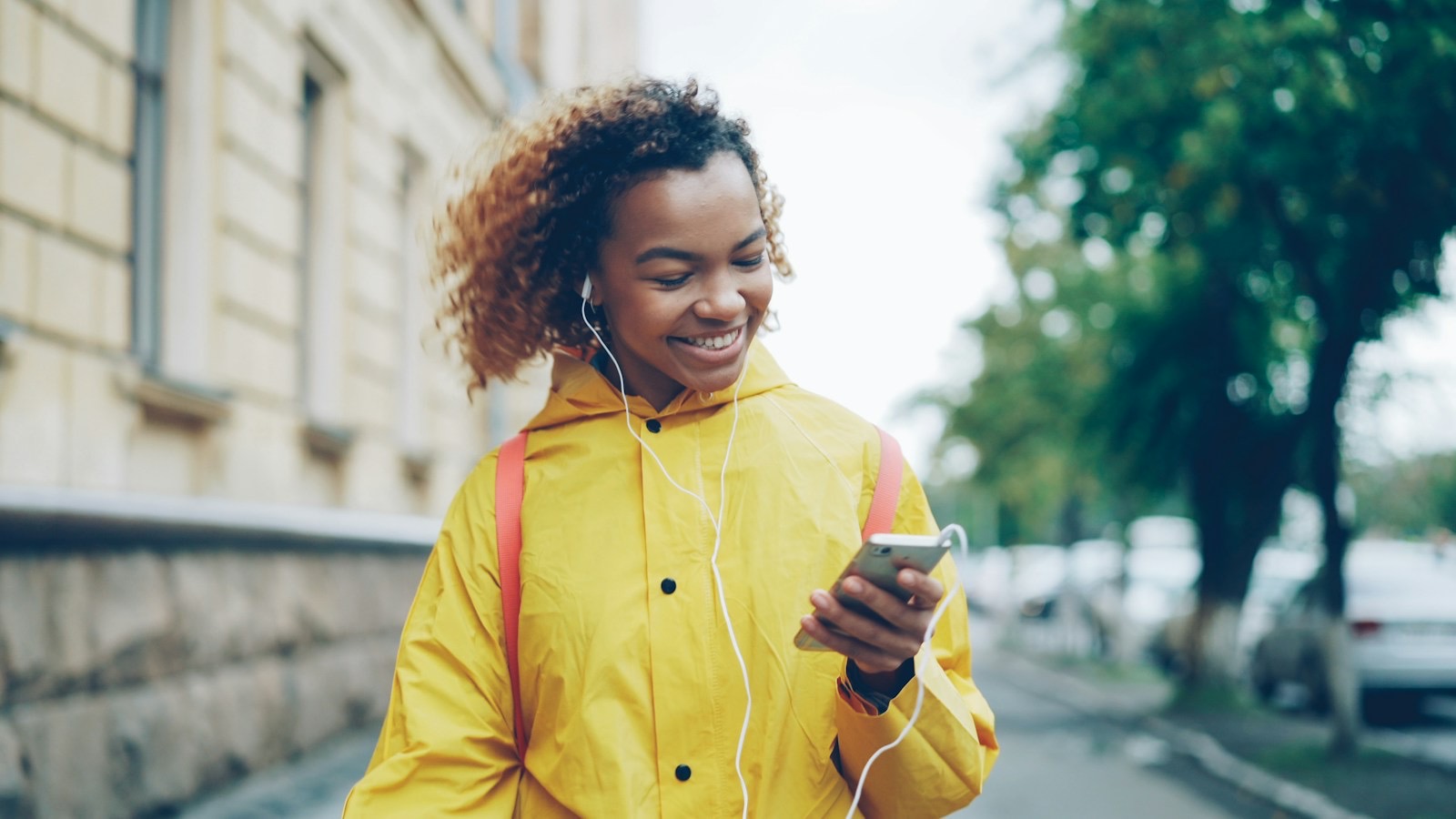 A smiling woman with earbuds looking at her phone