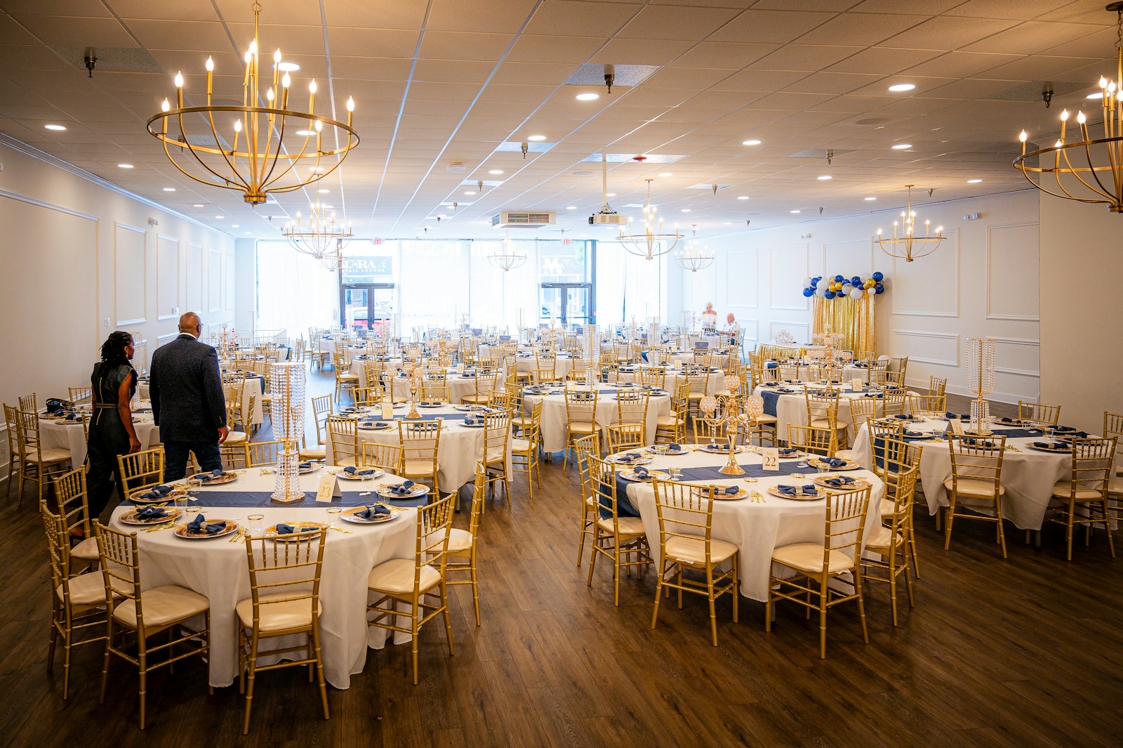 A hotel banquet hall set with round tables, gold chairs and chandeliers before an event